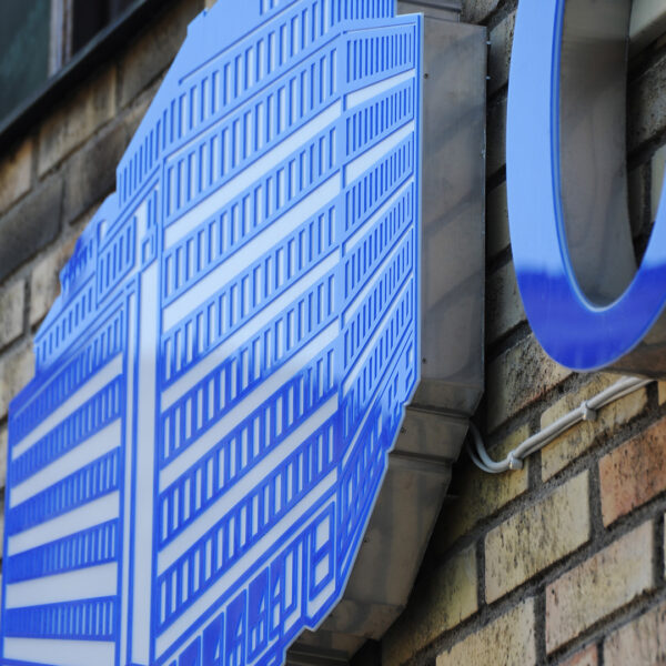 Fasadskylt med framifrån LED-belysta profilbokstäver i rostfritt stål, opalfronter med translucent vinyldekor och logotyp i blå urfräst akryl på vit akryl - Bild 4